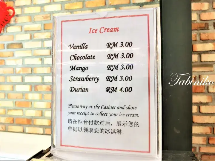 Ice cream menu displaying flavors and prices in Malaysian Ringgit against a brick wall background.