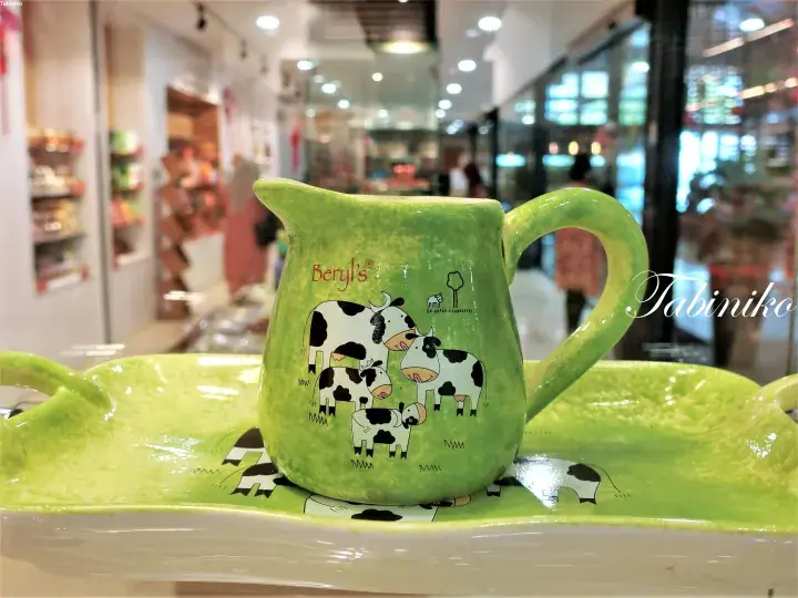 Green ceramic pitcher and tray with cow illustrations and Beryl’s logo displayed on a store shelf.