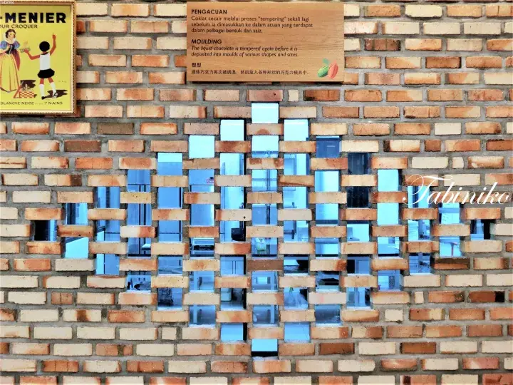 Decorative brick wall with mirrored gaps and a Menier chocolate sign at the Chocolate Museum in Ipoh.