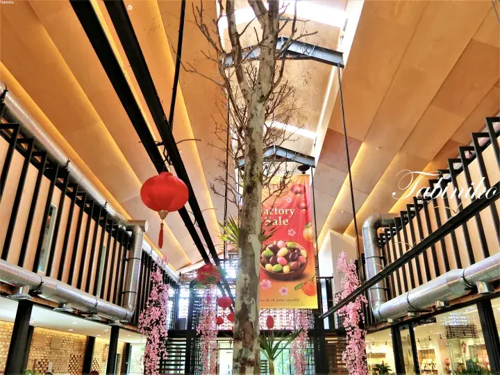 Interior atrium with hanging red lanterns, pink floral decorations, and a factory sale banner at a modern shopping mall.