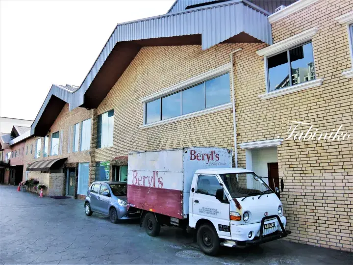 Beryl’s delivery truck parked outside a brick building with distinctive peaked roofs.