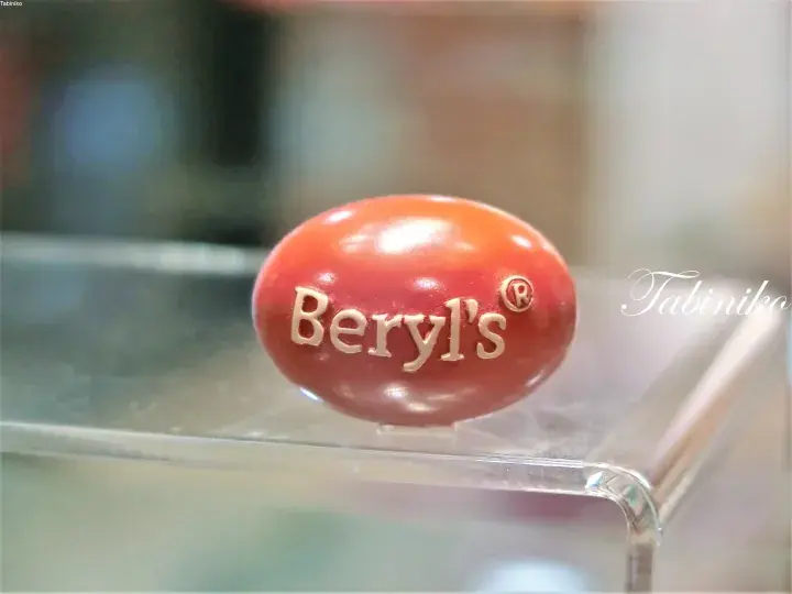 Close-up of a glossy red Beryl’s chocolate with the brand name embossed in gold, displayed on a clear acrylic stand.