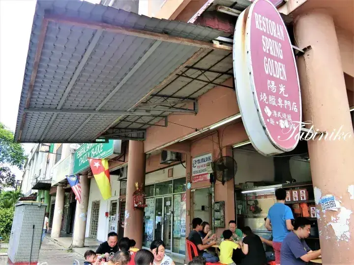 外で食事をする客と赤い楕円形の看板があるRestoran Spring Goldenの外観。