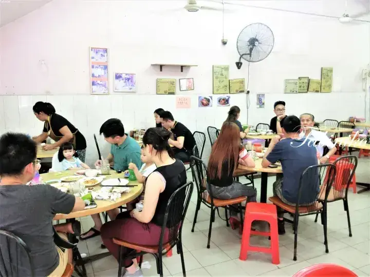 ラウンドテーブルと壁掛けファンが特徴のカジュアルな地元の飲食店で食事を楽しむ客たち。