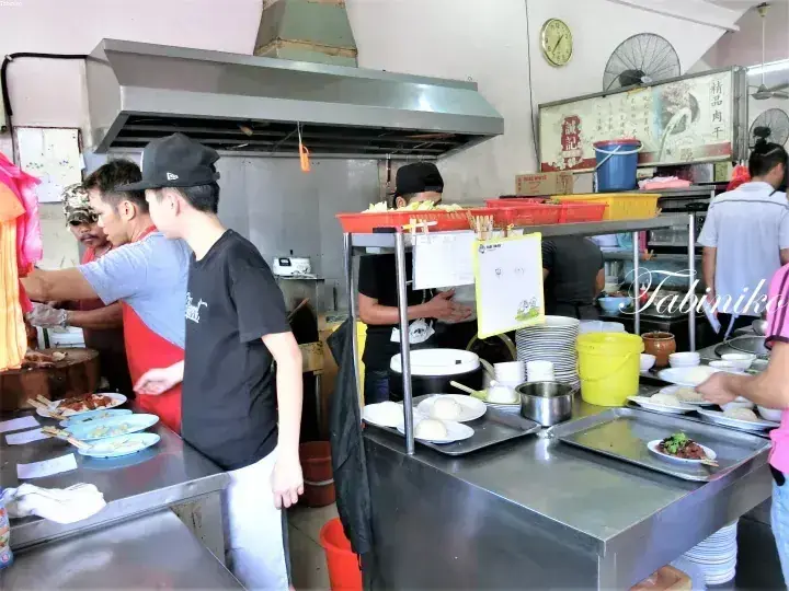 ステンレスの調理台で料理を作るスタッフと客で賑わうマレーシアの屋台の厨房。