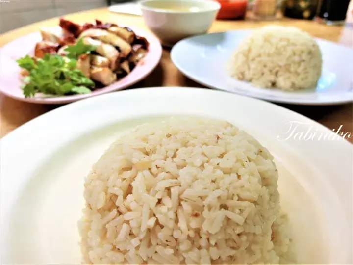 A plate of Hainanese chicken rice with a mound of fragrant rice and sliced chicken garnished with cilantro.