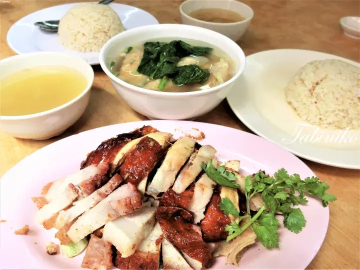 A plate of roasted and white meat with rice, soup, and wonton soup on a wooden table.