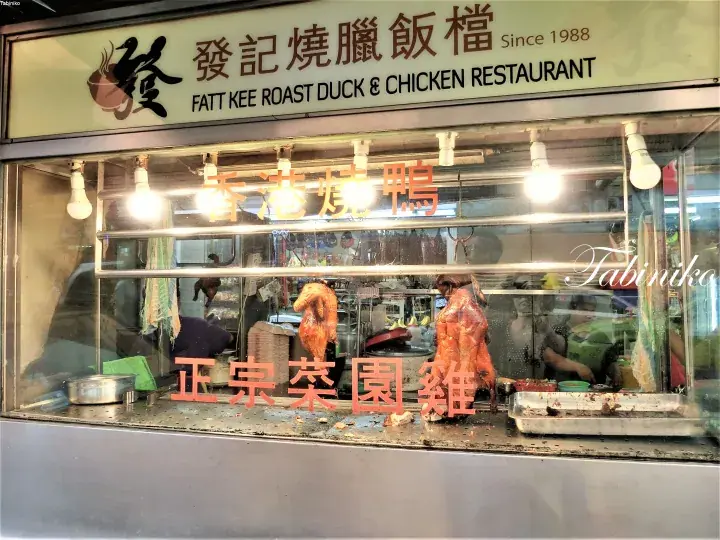 Fatt Kee Roast Duck & Chicken Restaurant storefront displaying roasted meats behind glass with neon signs.
