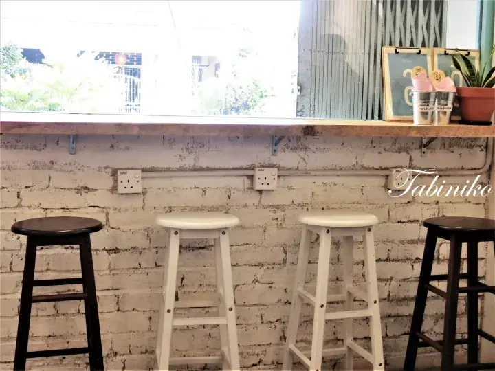 Bar stools lined up against a white brick wall under a window at Tabiniko cafe.