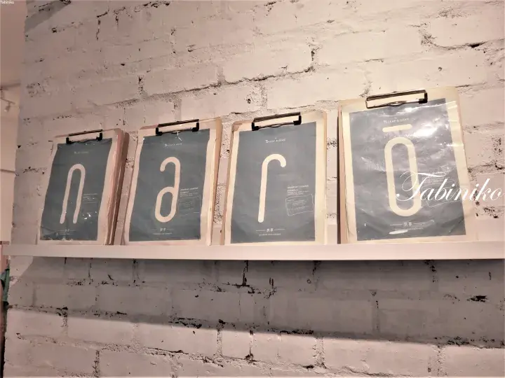 Four framed posters displaying the letters n, a, r, o on a white shelf against a painted brick wall.