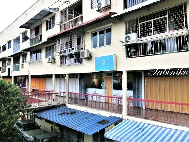 narōカフェとJabinikoレストランが並ぶ、エアコンや金網が設置されたショップハウス街の風景。