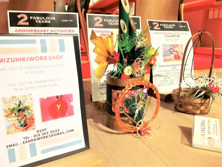 Mizuhiki Workshop display featuring a decorative Ikebana arrangement and event flyers for a 2nd anniversary celebration.