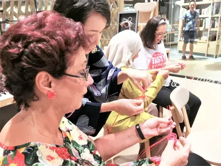 明るい空間で赤い糸の織り方を学ぶ女性たちのワークショップの様子。