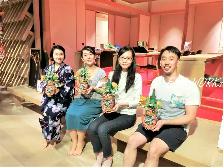 Four people sitting on a bench holding handmade flower arrangements in a room with pink walls.