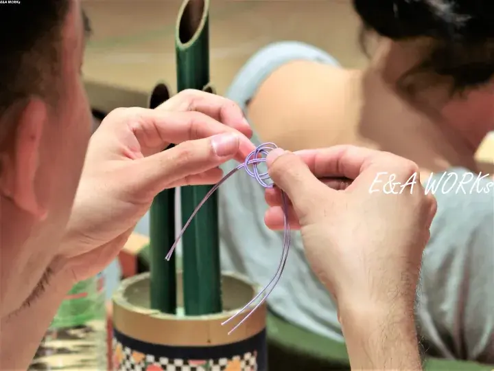 Hands weaving a purple cord knot during a craft workshop at E&A WORKS.