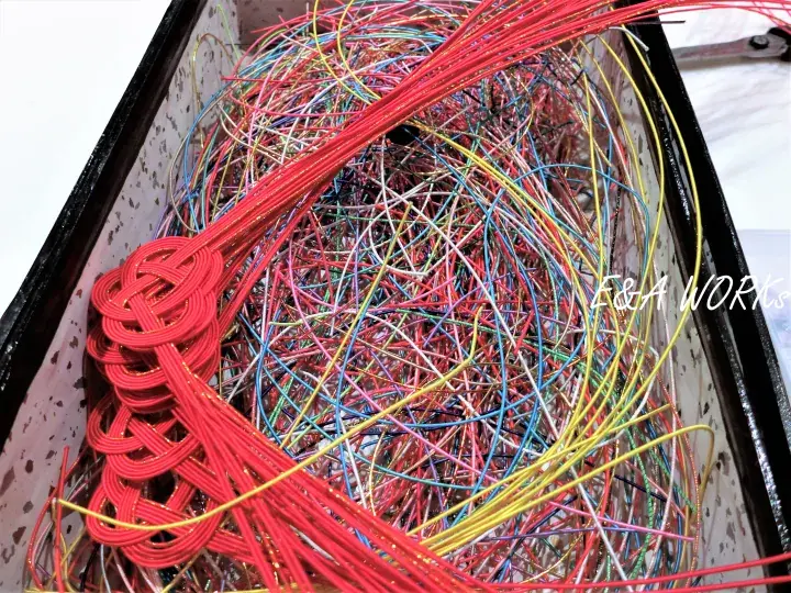 Colorful wires and red braided cords tangled inside a black container.
