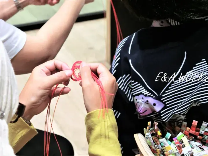 Hands weaving a red string bracelet at E&A Works workshop in Malaysia