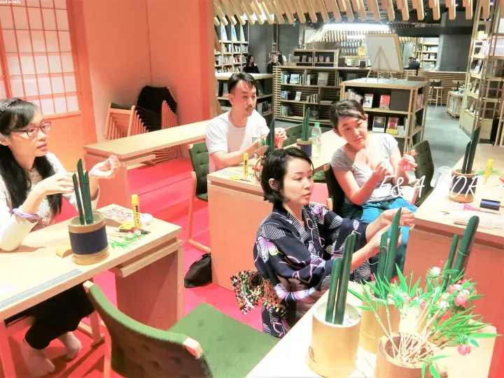 People participating in a cactus planting workshop at a modern bookstore with wooden shelves and warm lighting.