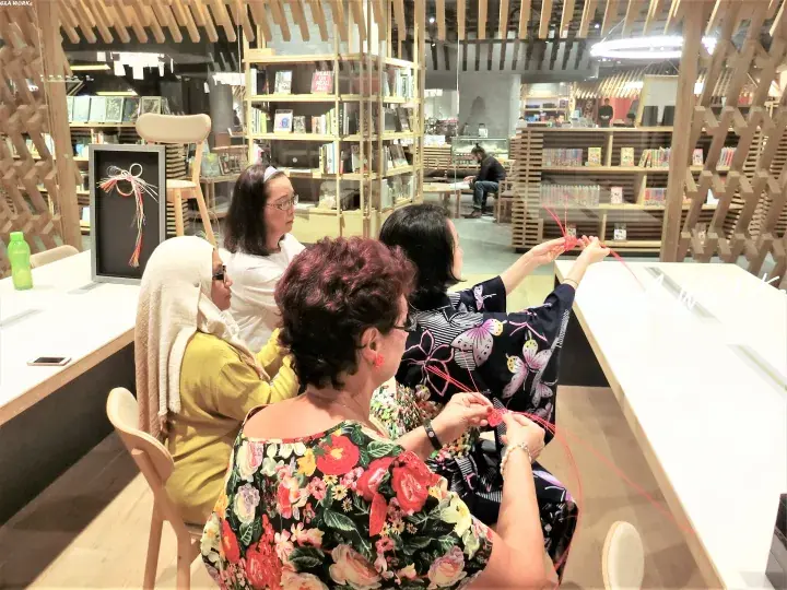 Women knitting at a table inside a bookstore with wooden lattice walls and bookshelves.