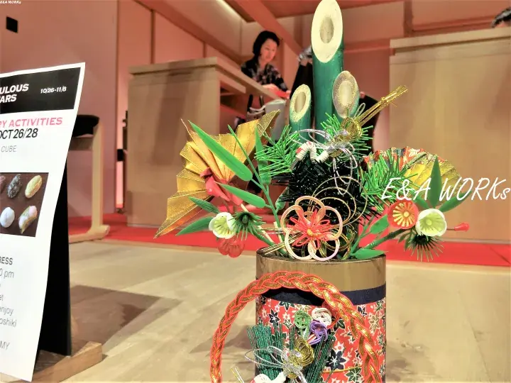 Colorful traditional Japanese New Year decoration with bamboo and flowers on a patterned stand at an event.