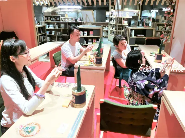 Guests participate in a traditional craft workshop at a vibrant indoor venue with wooden desks and shelves.