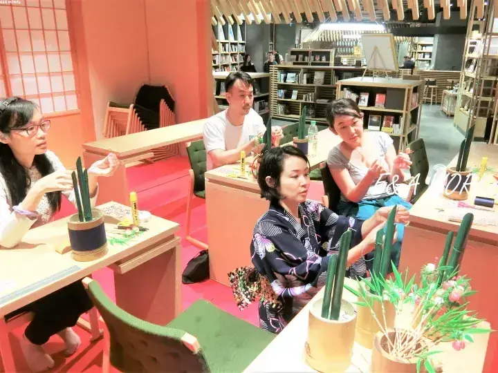 木製の棚と温かい照明が特徴的なモダンな書店で、サボテン植えのワークショップに参加する人々。