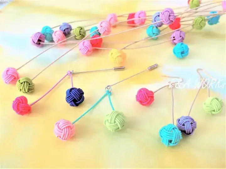 柔らかな黄色の背景に並べられた、カラフルな手作りの結び目ブローチ。