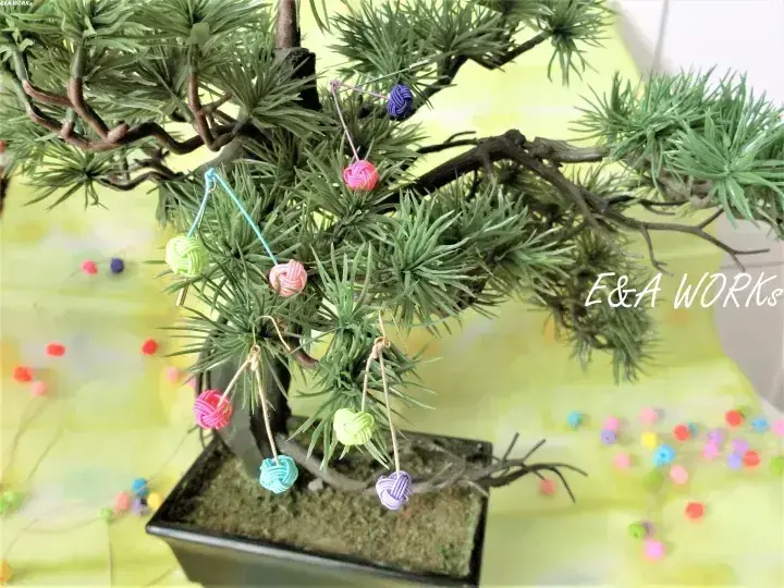 鉢植えのミニチュア盆栽に吊るされたカラフルな手作り編み飾り。