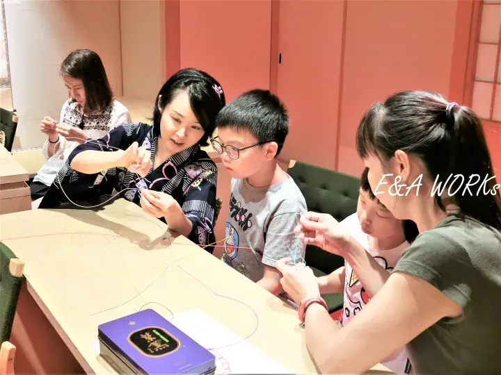 A group of people participating in a traditional craft workshop, learning embroidery techniques at a table.
