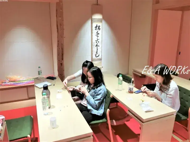 和室で木製のテーブルに向かい、三人の女性が色とりどりの糸を使って手作りに取り組んでいる様子。