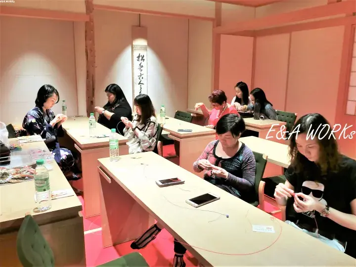 Participants at an E&A WORKS event focused on crafting, seated at tables with water bottles and tools in a warmly lit room.
