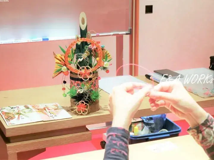 木製のテーブルに完成した正月飾りが置かれ、手元で新しい正月飾りの制作を行っているワークショップの風景。