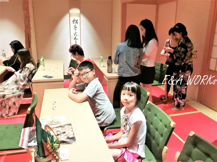 Children and adults in a Japanese-style room with tatami mats and calligraphy, enjoying a cultural experience.