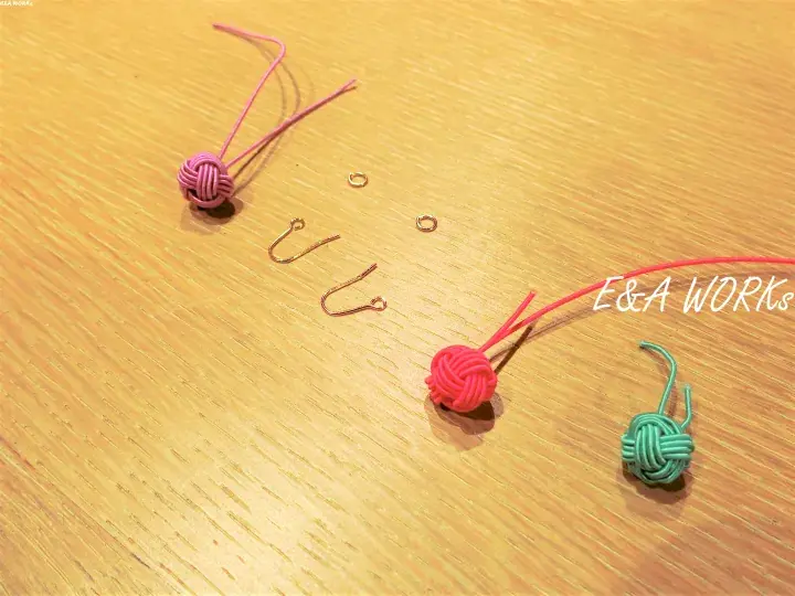 Colorful macrame knots and earring hooks arranged on a wooden surface for a DIY craft project.