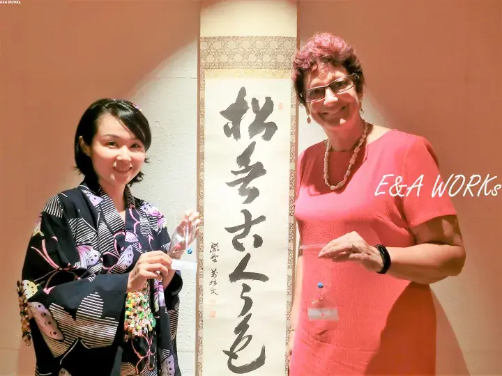 Two women posing with a Japanese calligraphy scroll at an E&A Works event.
