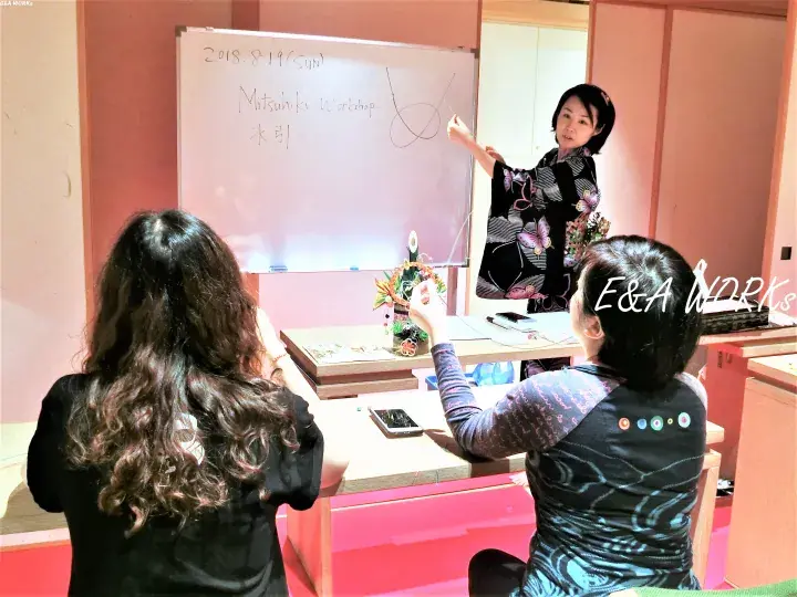 Instructor teaching a workshop at a whiteboard with ‘Mitsubishi Workshop’ written on it, attended by two participants.