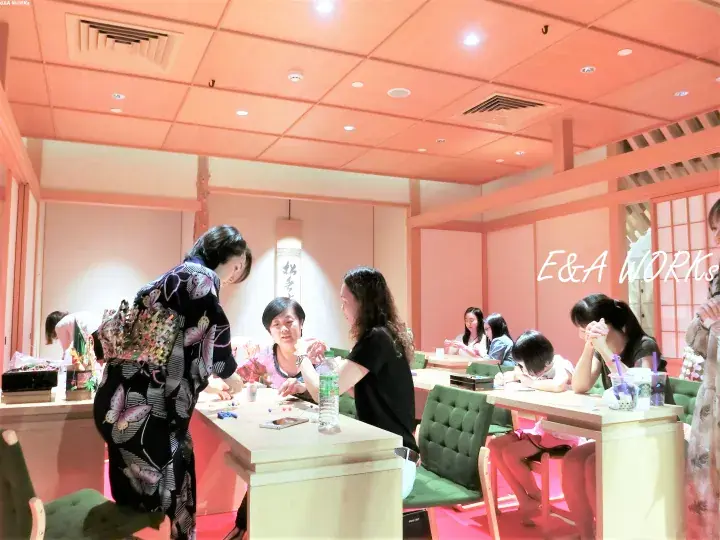 Guests in kimonos interact at a table in a pink-themed room with E&A Works branding visible on the wall.