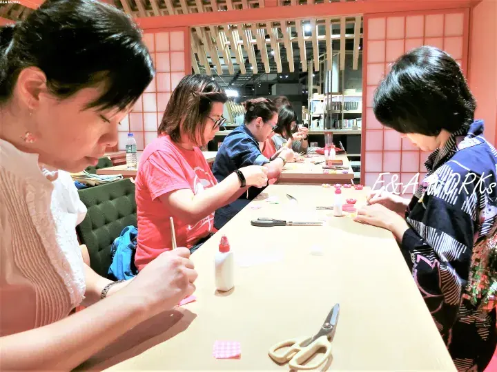 Women crafting at a long table in a Japanese-style room with shoji screens and wooden ceiling beams.