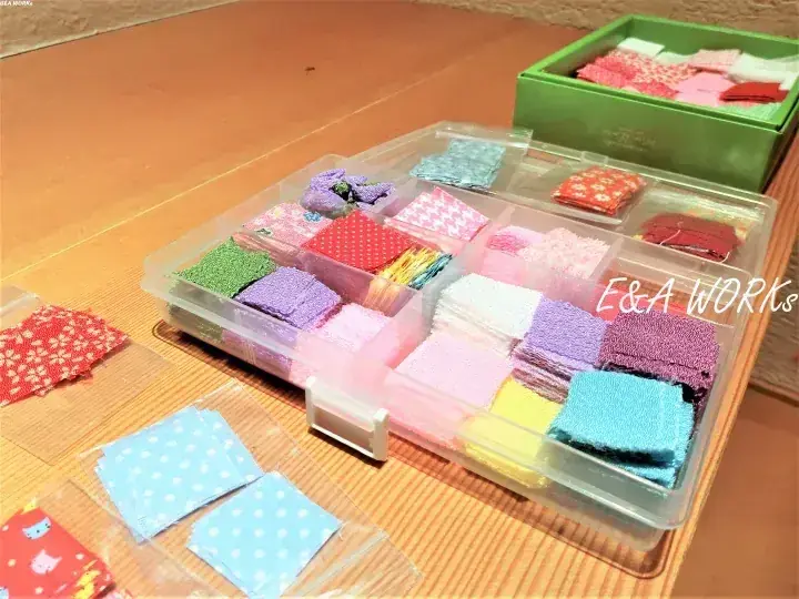 木製テーブルの上に置かれた、色とりどりの布切れや糸が整理されたプラスチック製収納ケース。