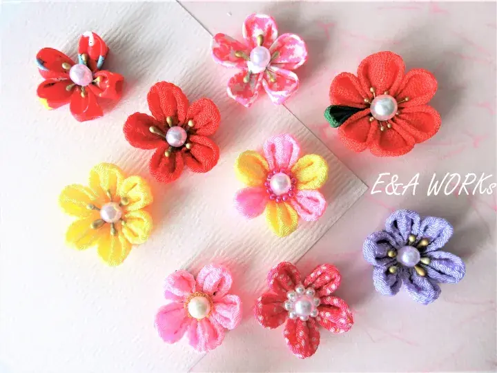 Colorful handmade fabric flowers with pearl centers arranged on a light wooden surface by E&A WORKS
