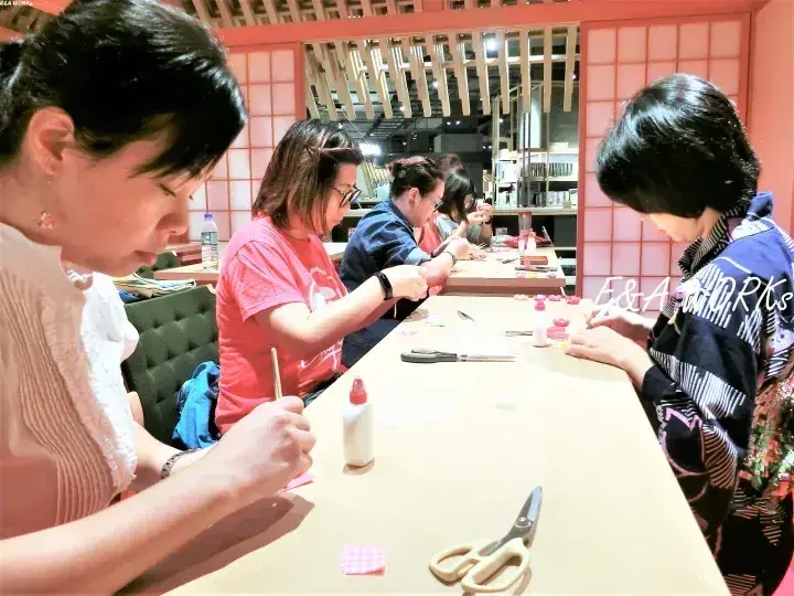 障子と木製天井が特徴的な和室で、長いテーブルを囲んで工作をする女性たち。