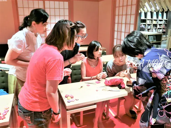Group of women gathered around a table in a Japanese-style room, engaging in a hands-on craft activity with fabric and scissors.