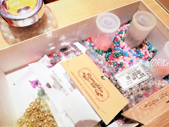 A box filled with colorful beads, gold charms, and SSF brand packaging for crafting supplies.