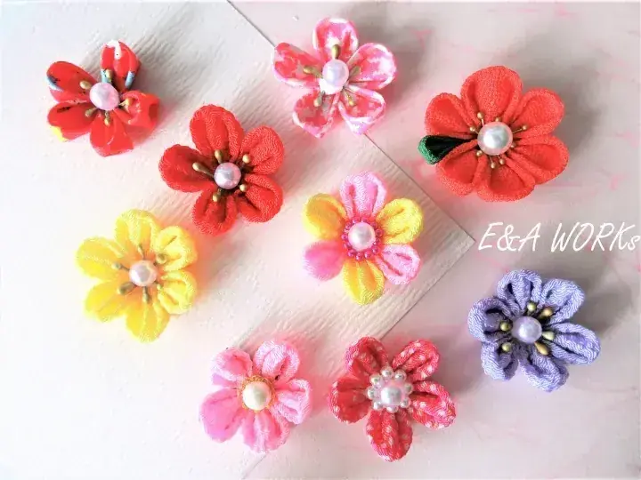 E&A WORKSによる真珠の中心を持つカラフルな手作りの布の花が木製の表面に並んでいる