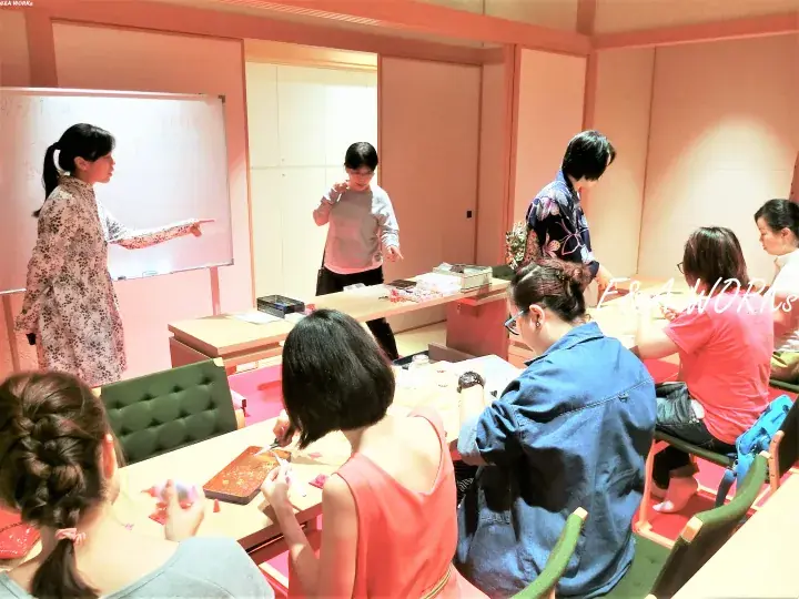 A group of women participating in a workshop at a table while one presenter points to a whiteboard in a pink room.