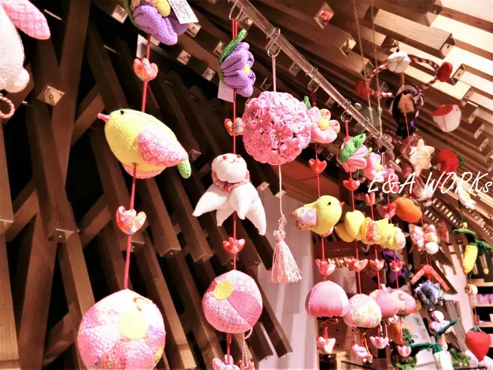 Colorful handmade plush toys hanging from wooden beams at L&A Works shop.