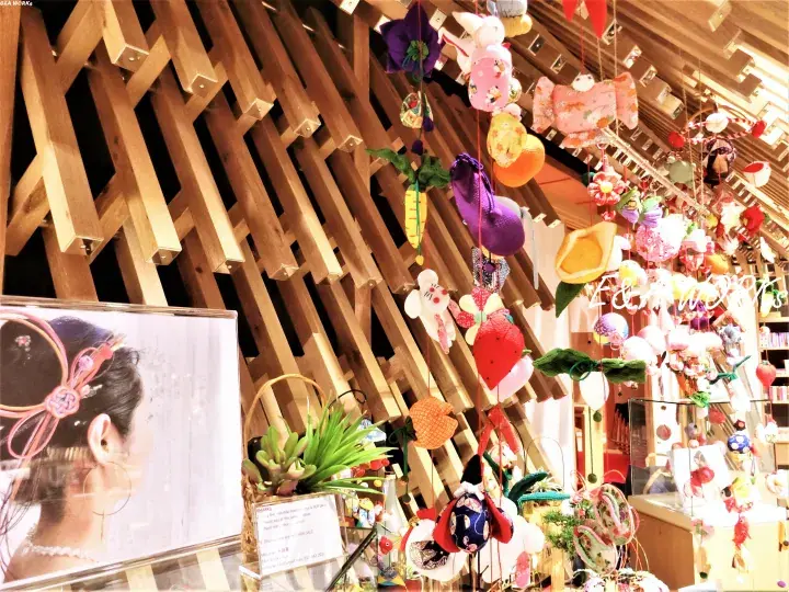 Colorful handmade fabric ornaments hanging from a wooden lattice ceiling in a Malaysian craft shop.