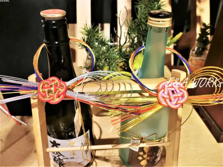 Two sake bottles in a wooden carrier decorated with colorful traditional Japanese cords and knots.