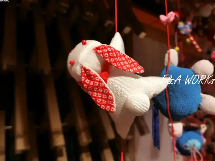 Handcrafted fabric bunny charm with red patterned ears hanging from a red string, part of E&A WORKS collection
