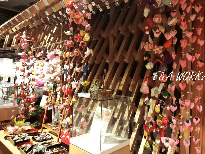 Colorful handmade ornaments hang from wooden beams at the E&A WORKS stall.